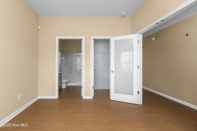 unfurnished bedroom with a walk in closet, baseboards, a closet, and wood finished floors