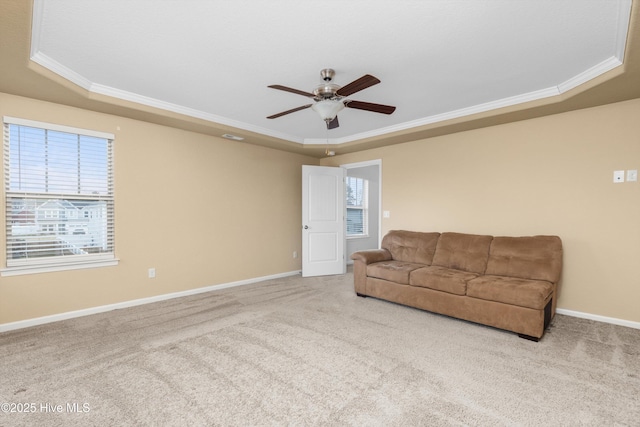 carpeted living room with a healthy amount of sunlight, a raised ceiling, a ceiling fan, and ornamental molding