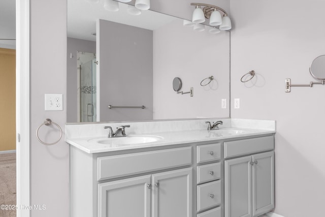 bathroom with double vanity, a shower with shower door, and a sink