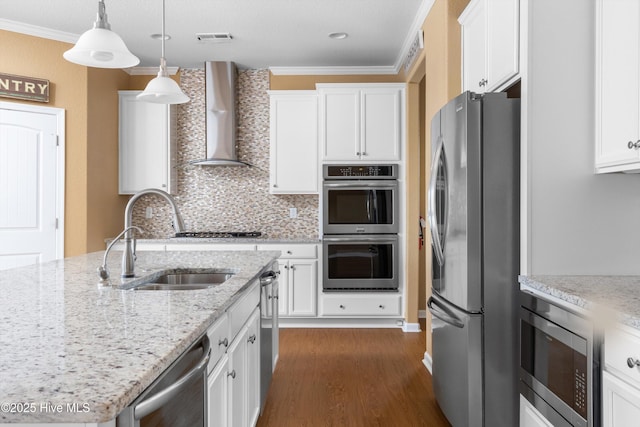 kitchen with visible vents, a sink, ornamental molding, stainless steel appliances, and wall chimney range hood