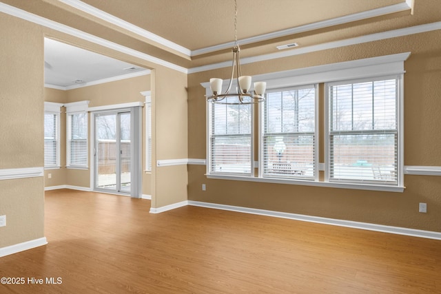 unfurnished dining area with baseboards, crown molding, an inviting chandelier, and wood finished floors