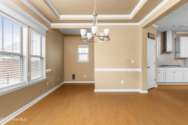 unfurnished dining area featuring baseboards, an inviting chandelier, crown molding, light wood-style floors, and a raised ceiling