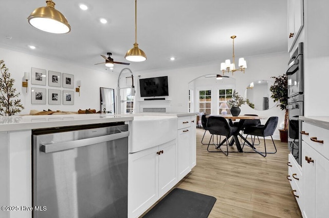 kitchen featuring white cabinetry, light wood-style flooring, ornamental molding, stainless steel dishwasher, and open floor plan