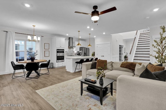 living area featuring light wood-type flooring, ceiling fan with notable chandelier, recessed lighting, crown molding, and stairs