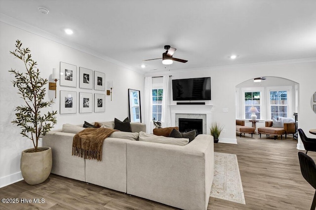 living room with a high end fireplace, crown molding, baseboards, wood finished floors, and a ceiling fan