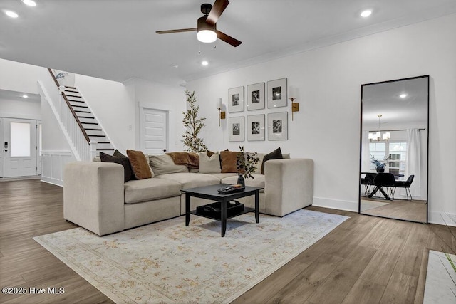 living area featuring ornamental molding, ceiling fan with notable chandelier, wood finished floors, recessed lighting, and stairway