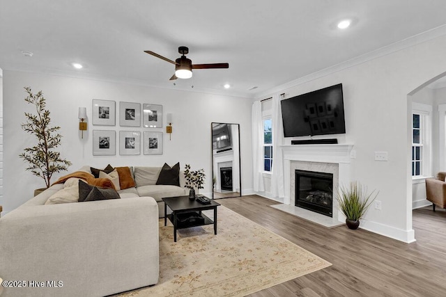 living area with arched walkways, a ceiling fan, ornamental molding, and a fireplace