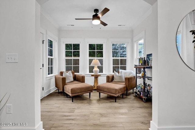 living area featuring visible vents, light wood-style flooring, a ceiling fan, and ornamental molding