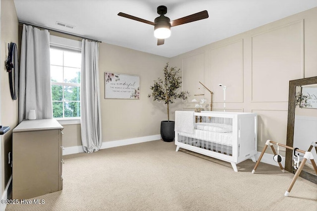 bedroom with visible vents, baseboards, light colored carpet, a decorative wall, and a ceiling fan