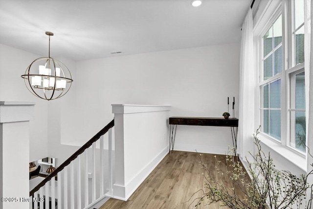 hall with visible vents, baseboards, an upstairs landing, wood finished floors, and a notable chandelier