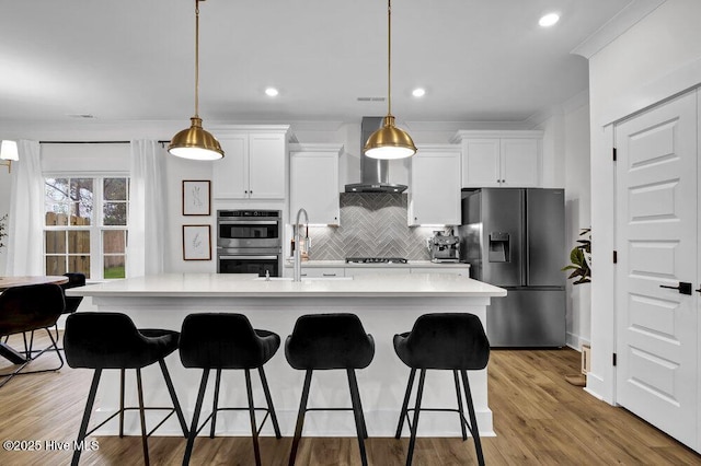 kitchen with a breakfast bar, light countertops, appliances with stainless steel finishes, wall chimney exhaust hood, and tasteful backsplash