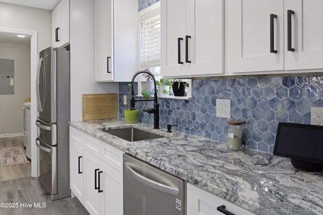 kitchen with light stone counters, appliances with stainless steel finishes, wood finished floors, white cabinetry, and a sink