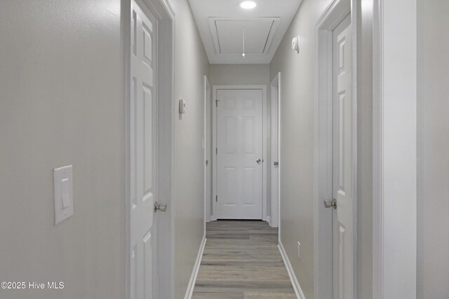 hall with attic access, light wood-style floors, and baseboards