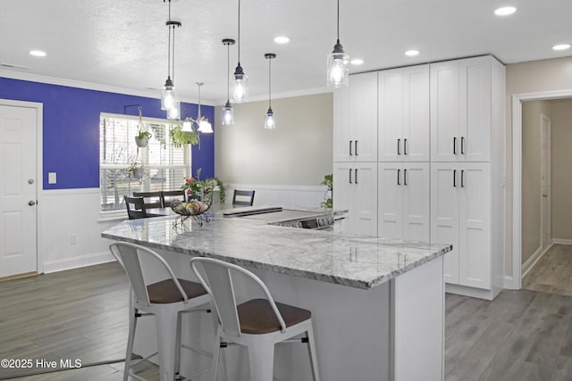 kitchen with white cabinetry, light stone counters, wood finished floors, and ornamental molding