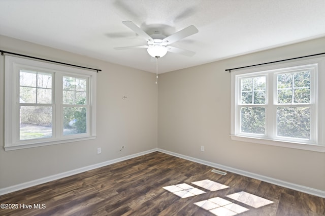 empty room featuring ceiling fan, visible vents, baseboards, and dark wood finished floors