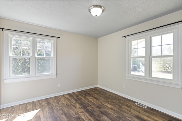 empty room with dark wood-style floors, visible vents, a textured ceiling, and baseboards