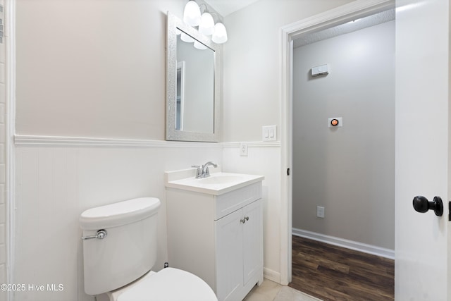 half bath featuring vanity, toilet, and wainscoting