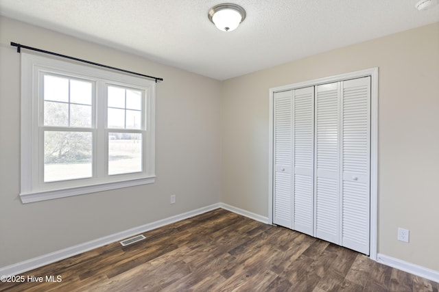 unfurnished bedroom with a closet, baseboards, visible vents, and dark wood-style flooring