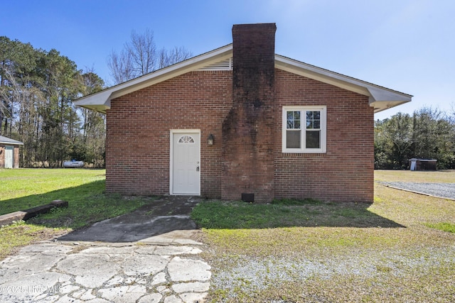 view of front of home with brick siding, a chimney, and a front yard