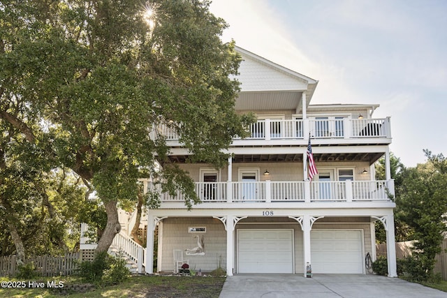 coastal inspired home featuring an attached garage, fence, stairs, a balcony, and driveway