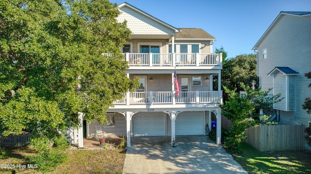 raised beach house featuring a balcony, an attached garage, driveway, and fence