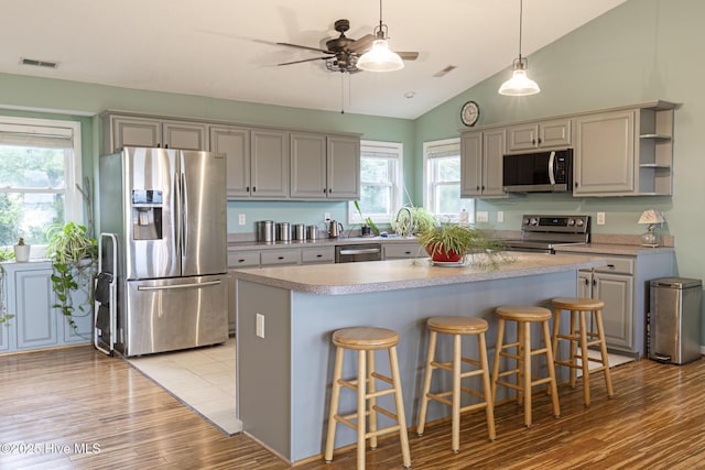 kitchen featuring a ceiling fan, light wood-style flooring, light countertops, appliances with stainless steel finishes, and a kitchen breakfast bar