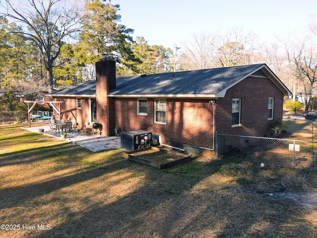 rear view of property featuring a patio, a chimney, central air condition unit, a lawn, and brick siding