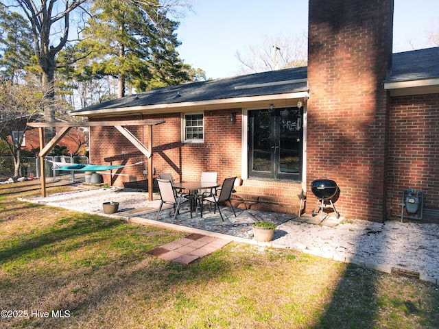 back of property featuring brick siding, a shingled roof, a lawn, a chimney, and a patio