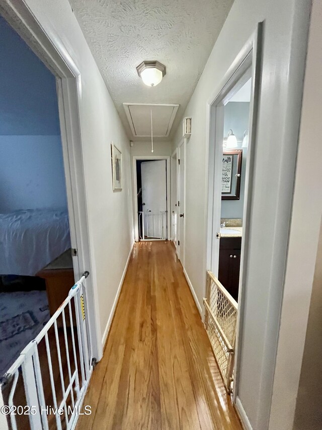 hallway with light wood-type flooring, baseboards, a textured ceiling, and attic access