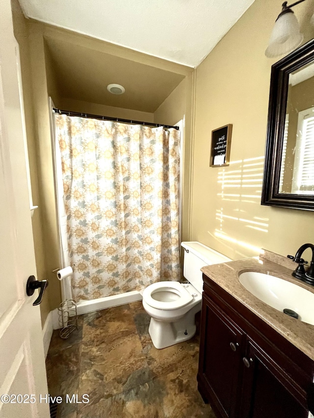 bathroom featuring vanity, toilet, a shower with curtain, and stone finish flooring