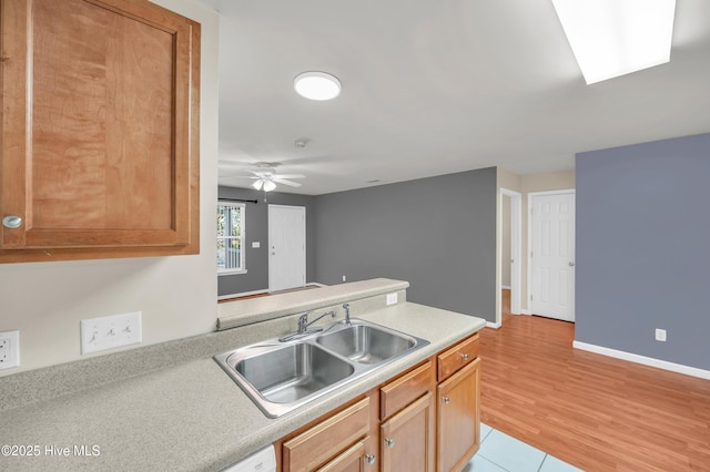 kitchen with a sink, light wood-style floors, a peninsula, light countertops, and ceiling fan