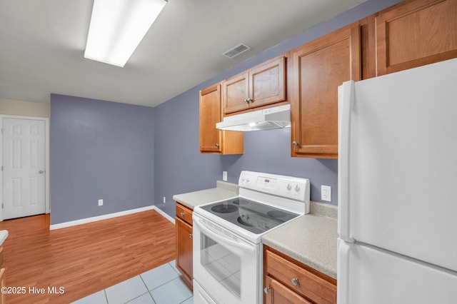 kitchen featuring visible vents, under cabinet range hood, white appliances, light countertops, and baseboards