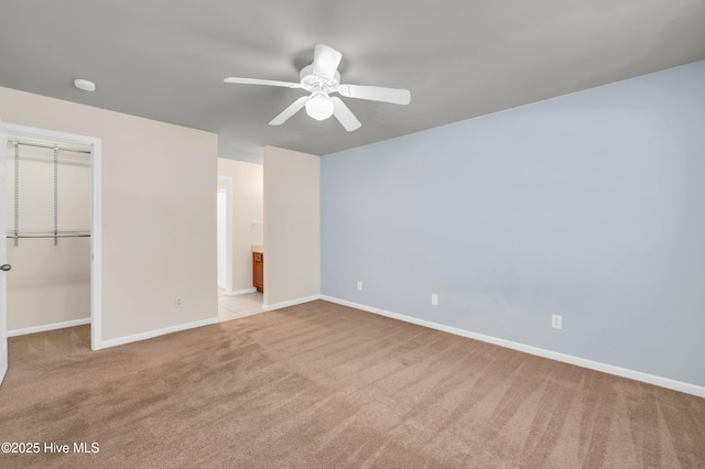 unfurnished bedroom with baseboards, a spacious closet, a closet, ensuite bathroom, and light colored carpet