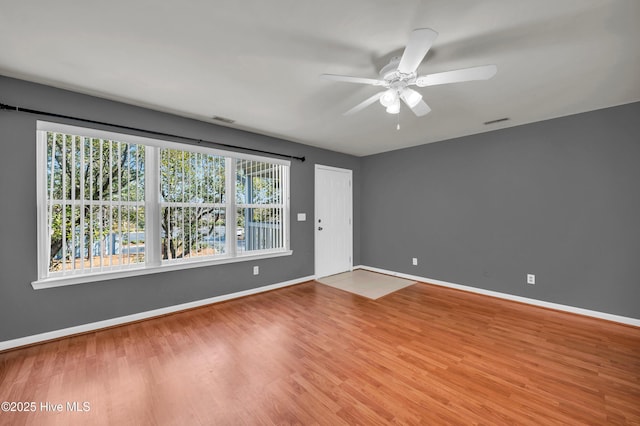 spare room featuring ceiling fan, visible vents, baseboards, and wood finished floors