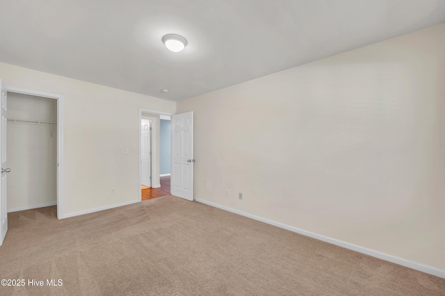 unfurnished bedroom featuring a closet, baseboards, light colored carpet, and a spacious closet