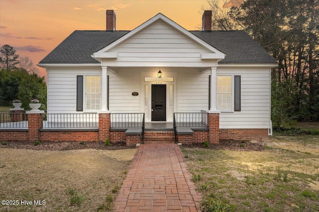 bungalow featuring a shingled roof, a porch, and a chimney