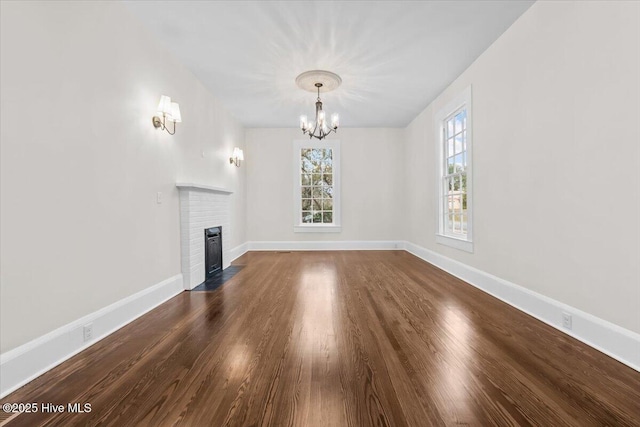 unfurnished living room with a fireplace, an inviting chandelier, dark wood-style floors, and baseboards