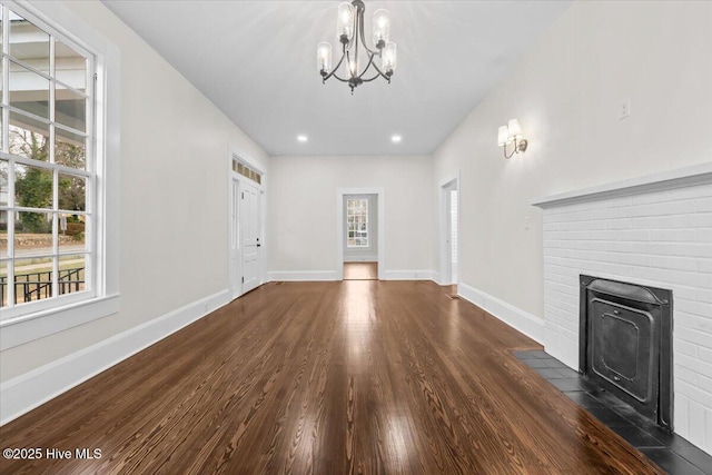 unfurnished living room featuring dark wood finished floors, an inviting chandelier, plenty of natural light, and baseboards