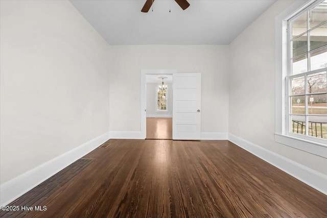 unfurnished room with baseboards, dark wood finished floors, and ceiling fan with notable chandelier