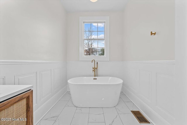 bathroom with visible vents, marble finish floor, wainscoting, a soaking tub, and vanity