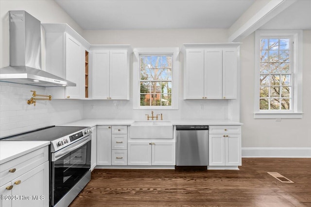 kitchen featuring visible vents, a sink, stainless steel appliances, white cabinets, and wall chimney range hood