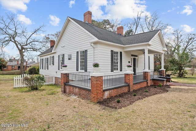 view of property exterior featuring covered porch, a chimney, a lawn, and a shingled roof