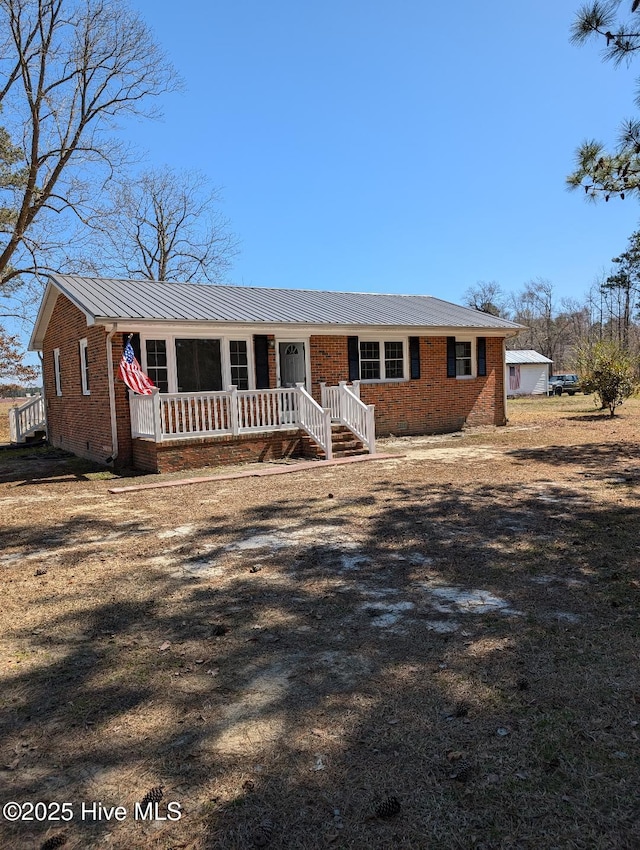 ranch-style house featuring metal roof, covered porch, brick siding, and crawl space