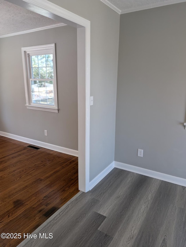 unfurnished room with visible vents, ornamental molding, a textured ceiling, dark wood finished floors, and baseboards