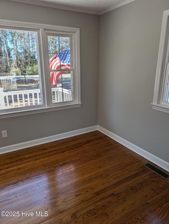 spare room featuring visible vents, crown molding, baseboards, and dark wood-style flooring