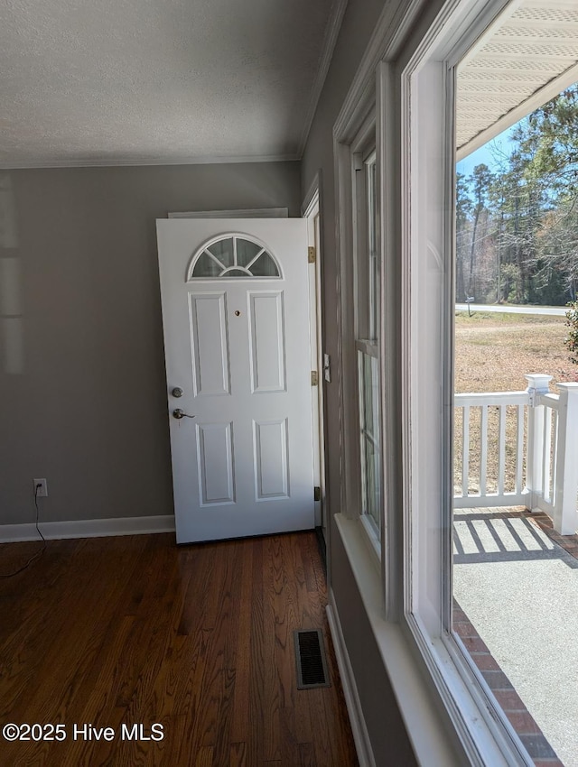 doorway to outside featuring baseboards, visible vents, dark wood finished floors, a textured ceiling, and crown molding