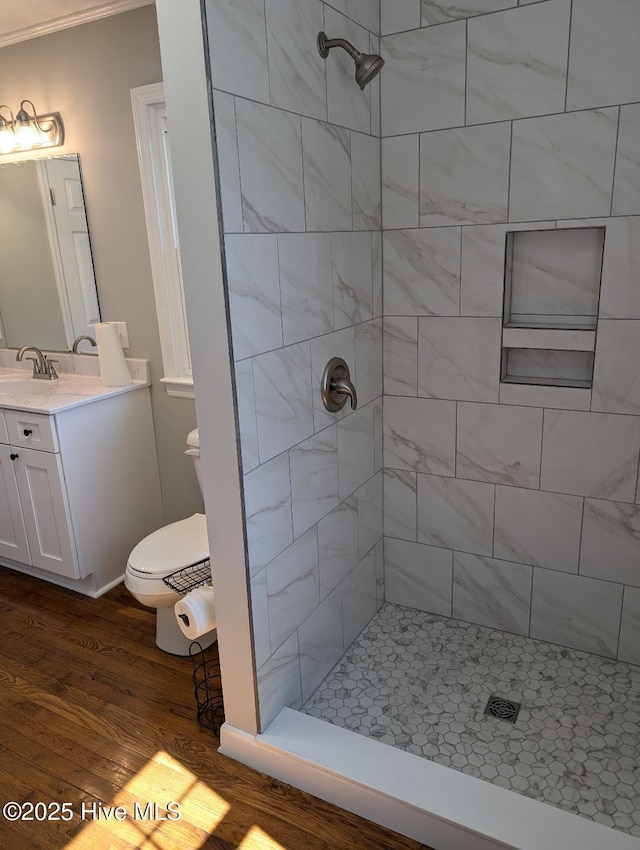 bathroom with a tile shower, toilet, vanity, and wood finished floors