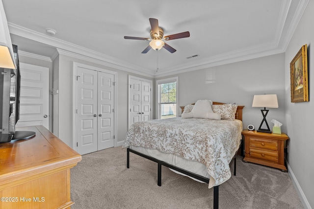 carpeted bedroom with a ceiling fan, baseboards, visible vents, ornamental molding, and two closets