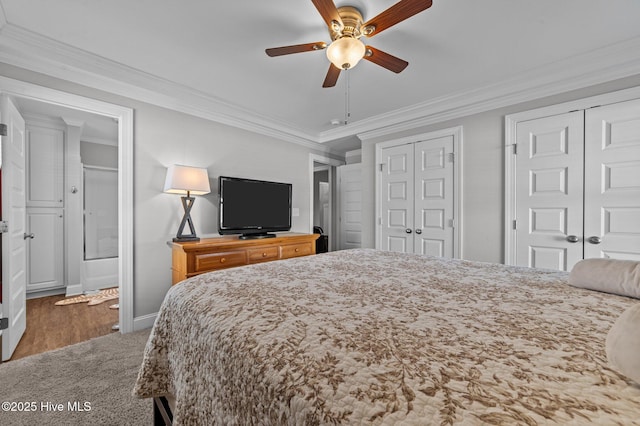 carpeted bedroom with two closets, crown molding, baseboards, ensuite bathroom, and a ceiling fan