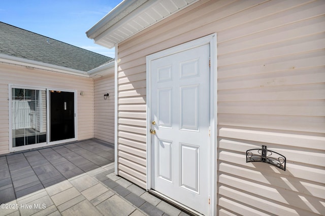 property entrance with a patio area and roof with shingles